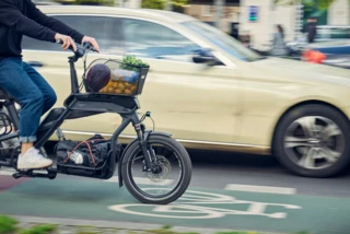 Jemand fährt mit einem Ca Go CS auf einem Fahrradweg in der Stadt. Daneben fährt ein Auto.