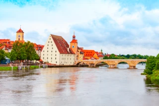 Blick auf die Donau. Im Hintergrund sind weiße und rote Häuser zu erkennen. Eine Steinbrücke führt über den Fluss.