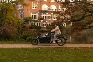 Eine Frau fährt mit dem Ca Go FS200 Life über einen Fahrradweg. Es ist Herbst, auf der Wiese liegt Laub. In der Box sitzt ihr kleiner Sohn.