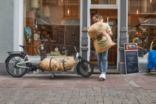 Ein Mann trägt einen großen Sack auf einem Geschäft. Davor steht ein FS Vario, das bereits mit einem Sack beladen ist.