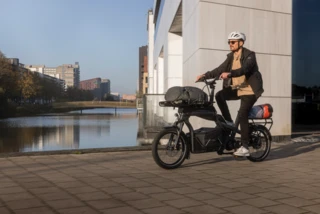 Ein Mann fährt mit dem Ca Go CS an einem Fluss entlang- Das Fahrrad ist mit einigen Gepäckträgern und Taschen ausgestattet.