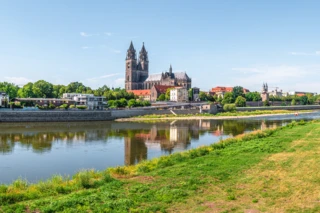 Die Elbe von einer Wiese aus fotografiert. Im Hintergrund ist eine Stadt mit einer großen Kirche zu erkennen.